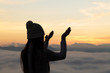 © Tinnakorn - Silhouette off   young woman praying for God's blessings with the power and power of the sacred On the background of sunrise. The concept of God and spirituality.