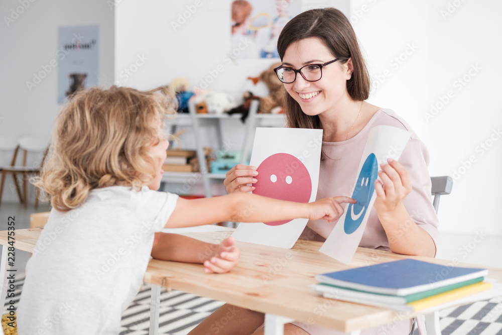 Smiling counselor holding pictures during meeting with young patient with autism - obrazy, fototapety, plakaty 