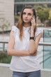 Young european female with brown hair, in white blouse and blue jeans calling via mobile phone with very concentrated and attentive face expression. Communication and mobile phone calls