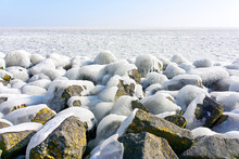 Snow And Ice Covered Granite Stones In Front Of An Ice Covered Sea In Winter Under A Blue Sky   