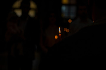 Wall Mural - burning candle in a Christian church. a blurred background of a church and a candle during a Christian ritual, such as a wedding or a baptism. natural light and noisy effect.looking for a dark effect.