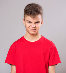 Wall Mural - Emotional portrait of caucasian upset problem teen boy. Sad boy looking at camera. Worried  child wearing red t-shirt, on gray background.