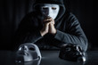 Hoodie man wearing mystery mask choosing black or white mask on the table. Anonymous social masking. Major depressive disorder or bipolar disorder. Halloween concept