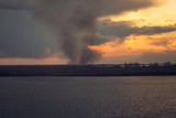 Fototapeta Storczyk - environmental problem of fire on dry grass with smoke onthe horizon inflated by a strong wind during the sunset