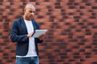 © Friends Stock - Using gadget. Young guy standing on wall browsing internet on digital tablet concentrated