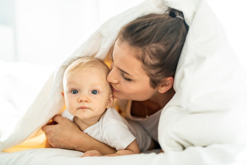 portrait of young mother with infant baby girl liying on the bed covered with a white blanket