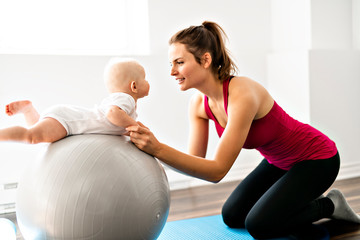 Poster - A Portrait of beautiful young mother in sports wear with her charming little baby in training session