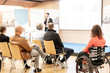 © kasto - Rear view of nrecognizable woman on wheelchair participating in business conference talk. Business and entrepreneurship symposium. Speaker giving talk at business meeting. Audience in conference hall.