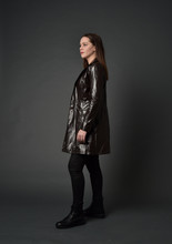 Full Length Portrait Of Brunette Girl Wearing Long Leather Coat And Boots. Standing Pose  On Grey Studio Background.