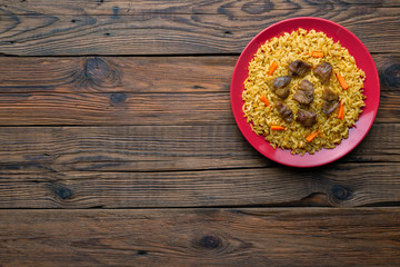 Wall Mural - Red plate with pilaf on a brown wooden table. On the table is red pepper, green onions, garlic, cherry tomatoes, red napkin, spoon. Top view. Flat lay.