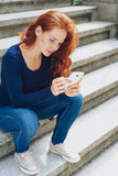 Fototapeta Na drzwi - Young woman sitting on steps with mobile phone