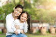 © ChayTee - Portrait of young happy asian mother and little cute daughter smiling, sitting and looking at camera at outdoor public nature park with copy space in family bonding and casual relax lifestyle concept.