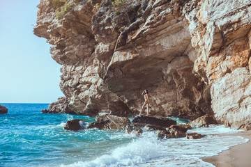 Wall Mural - Romantic passion young girl in bikini outdoors against wild tropical sea background. Beautiful sensual brunette mixed race Asian Caucasian woman with slim sporty tanned body standing on rock in water