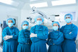 © DragonImages - Asian surgical team in masks and uniform keeping arms crossed and looking at camera while standing in operating theatre together