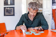 © Westend61 - Mature man sitting at table at home looking at notepads
