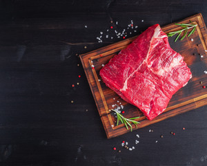 Wall Mural - Big whole piece of raw beef meat with seasoning on chopping board on dark background , copy space, top view