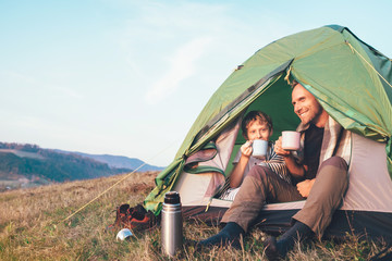 family lisure concept image. father and son drink a tea sitting in touristic tent