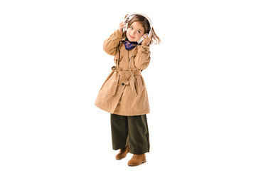 Wall Mural - happy little child in trench coat listening music with headphones isolated on white