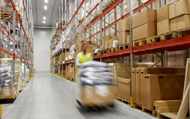 logistic business, shipment and loading concept - motion blurred picture of worker carrying loader with goods at warehouse