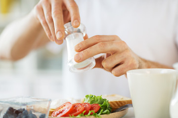 food, eating and people concept - close up of male hands seasoning breakfast by salt mill