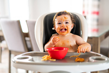 child girl, eating spaghetti for lunch and making a mess at home in kitchen