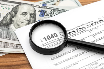 Magnifying glass on tax form and money on the table. Close up.