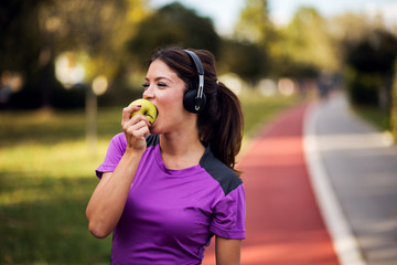 Fitness woman listening music with headphones and eating green apple