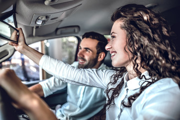 Wall Mural - Beautiful couple is looking at rearview mirror and smiling while sitting in their new car