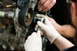 A young woman wearing white gloves uses a spanner while replacing the timing belt on a car engine.