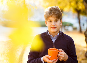 boy holds orange cup in hands on fallen leaves background. autumn mood beautiful day. Golden fall in still life. Bright Fall image.  