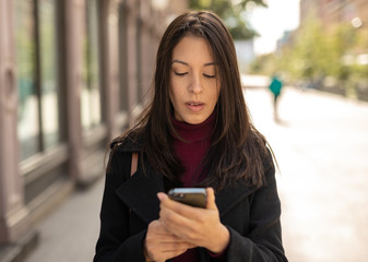 Wall Mural - Young woman in city using cell phone walking