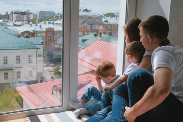 Family mom, dad and two twin brothers toddlers look out the window at the city.