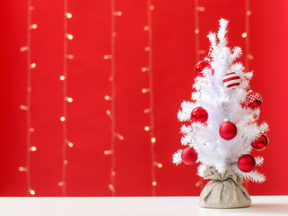 Wall Mural - Small white christmas tree with baubles on a shiny light red background