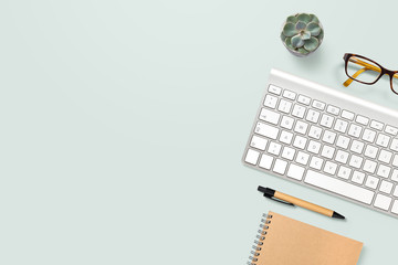 neat and clean, well organized home office workspace with technical gadgets, writing supplies, computer keyboard, glasses and a potted succulent plant on a mint background