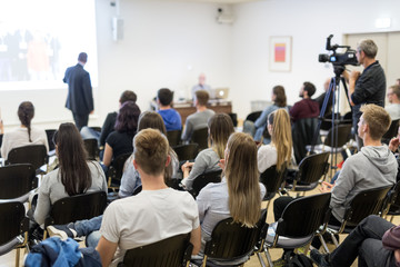 speaker lecturing in lecture hall at university. students listening to lecture and making notes.