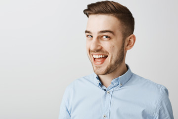 Wall Mural - Studio shot of amused mysterious handsome guy with bristle and stylish haircut hinting at something awesome smiling broadly and gazing at camera as if having interesting plan in mind