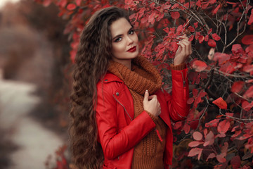 Wall Mural - Pretty Woman autumn outdoor portrait. Young beautiful brunette in leather jacket and warm woolen knitted sweater posing in red leaves park. Attractive girl in casual clothes smiling at camera.