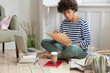 © WHstudio Leushin N - Photo of financial manager creats report in cozy place, sits crossed legs near opened laptop, holds papers, develops strategy for making business, uses books, drinks coffee, sits in modern apartment