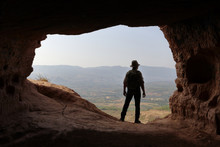 ISOLATED MAN WITH BACKPACK AND HAT AT THE ENTRANCE OF A CAVE