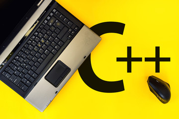 c++ programming language,. laptop and vertical mouse on yellow background with c++