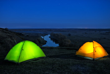 Wall Mural - lighted from the inside orange and green tents on hill above riv