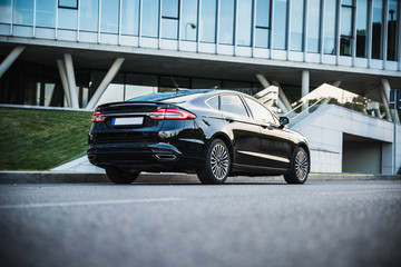 Luxurious black sedan in front of modern building