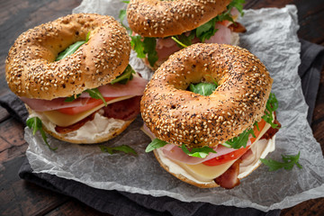 Wall Mural - Fresh Bagels Sandwiches with cream cheese, bacon, tomato and green wild rocket on rustic wooden table