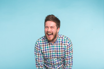 emotion, people and fun concept - young handsome man laughing on blue background