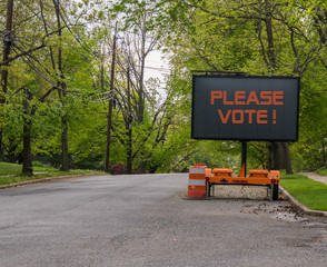 Please Vote electric LED sign on trailer on suburban street lined with trees