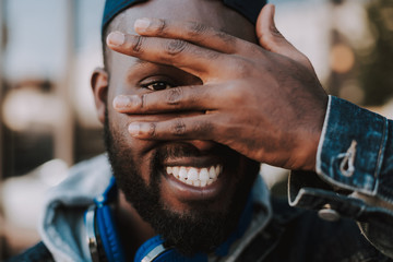 Wall Mural - Portrait of an overjoyed young afro american man holding his palm on the face while smiling