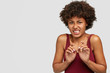 Discontent Afro girl with displeased expressions, feels disgust, frowns face and keeps hands near chest, poses against white background with free space for your advertisement. Fie, take it from me