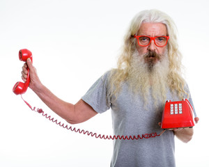 Studio shot of senior bearded man holding old telephone while lo