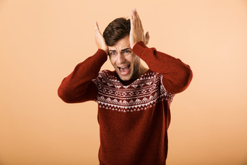 Canvas Print - Image of caucasian man 20s with stubble wearing knitted sweater screaming and expressing outrage, isolated over beige background