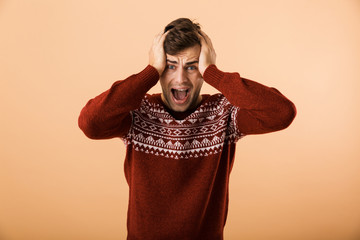 Canvas Print - Image of caucasian man 20s with stubble wearing knitted sweater screaming and expressing outrage, isolated over beige background